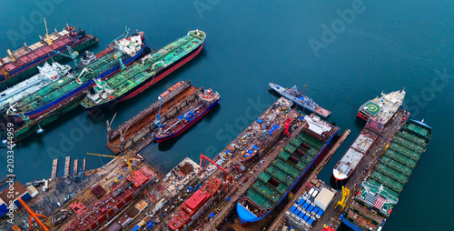 Wide aerial view displaying multiple huge cargo vessels and oil tankers moored side by side at an industrial shipyard facility alongside extensive deep blue sea water