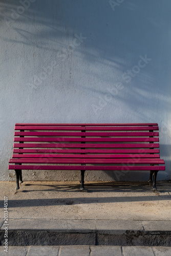 Banca de madera color rosa con estructura de herrería con fondo de muro blanco.