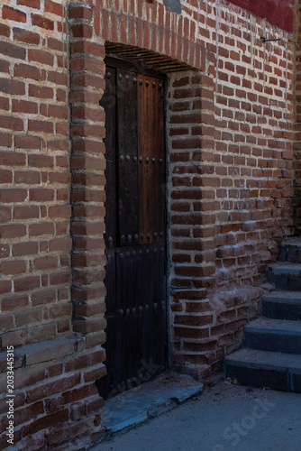 Muro y puerta de ladrillo rojo con puerta de madera con remaches, en calle con escalones.
