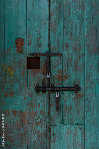 Puerta antigua de madera color azul turquesa, desgastada, con cerrojos de hierro.
