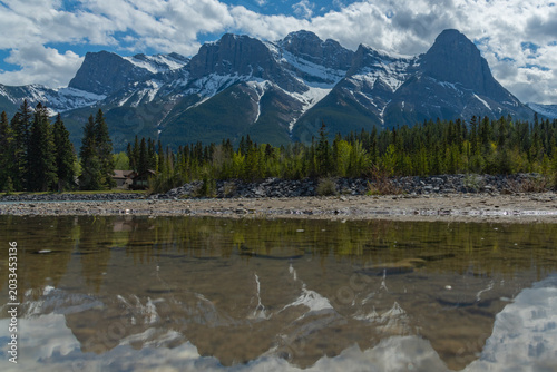 Stunning summer landscape of the Canadian Rocky Mountains and a calm river in Canmore, Alberta. Near Banff National Park with towering mountain peaks, Three Sisters. 