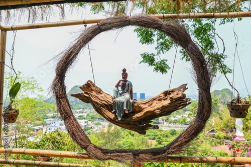 Bild auf Leinwand Beautiful Guanyin Bodhisattva statue sitting on driftwood swing inside a woven v
