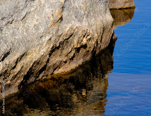 Tableau sur toile Textured grey rock overhang reflecting beautifully in the clear blue waters belo
