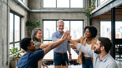 Diverse business team celebrating success in modern office with high fives and smiles