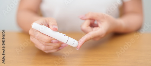 Fotografija Hand using lancet pen on finger with Blood drop glucose testing or Diabetes checking by digital blood glucose meter