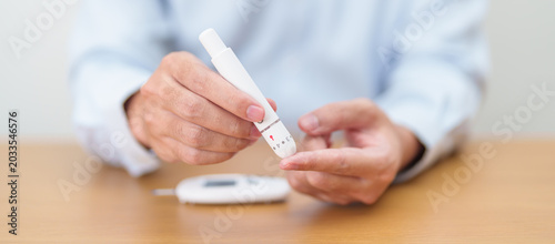 Fotografie Hand using lancet pen on finger with Blood drop glucose testing or Diabetes checking by digital blood glucose meter
