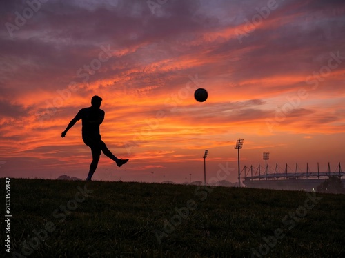 Silhouette of a soccer player kicking a ball at sunset