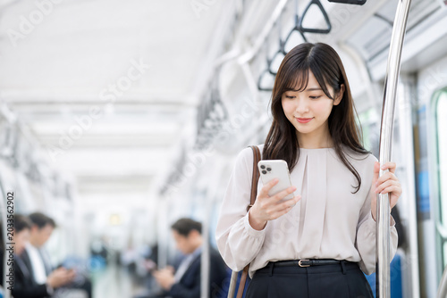 Tapety artystyczne 電車内でスマートフォンを見る笑顔の日本人女性