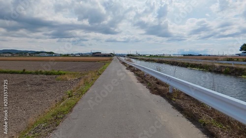 POV shot of moving forward on a straight path between a river and a rice field