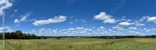 Panel kuchenny z motywem View of an expansive blue sky filled with fluffy white clouds over a lush green landscape with grassy fields and distant trees