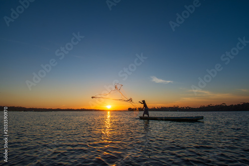 Photos Silhouette of a traditional Indonesian fisherman casting a net from a boat during a golden sunset