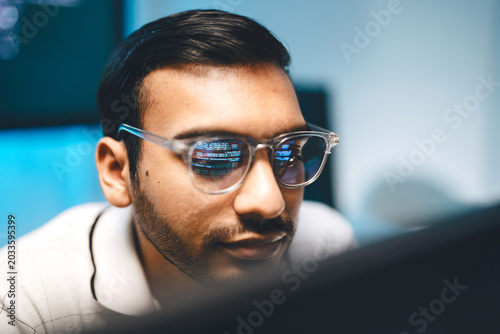 Close-up indian man tech engineering programmer eyeglasses with reflections computer machine learning code on the lenses