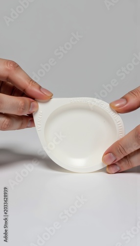 Close-Up of Hands Holding White Sealed Plastic Container Against Neutral Background