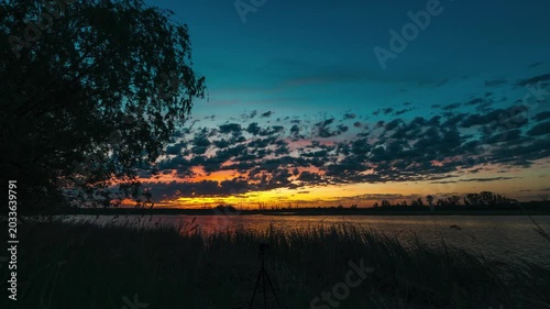 Sunset over a lake with beautiful clouds, timelapse of quickly flying clouds in the sky and the setting sun behind the horizon