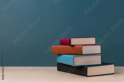 A stack of books on a white wooden desk against a green chalkboard background. Back to school, education levels, learning progress concept. Copy space for text.