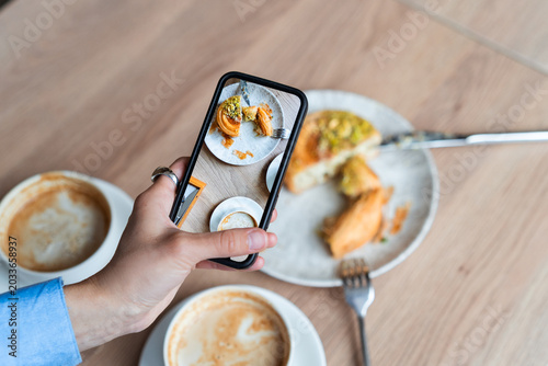 High angle view of a person holding a smartphone and taking a mobile photo of a breakfast table with coffee and pastry