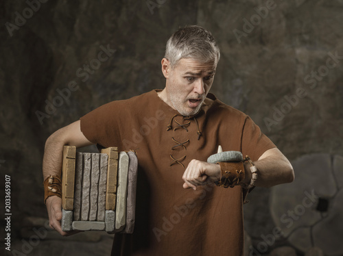 Cuadro en lienzo Stressed Prehistoric Businessman Checking Watch and Carrying Stone Documents