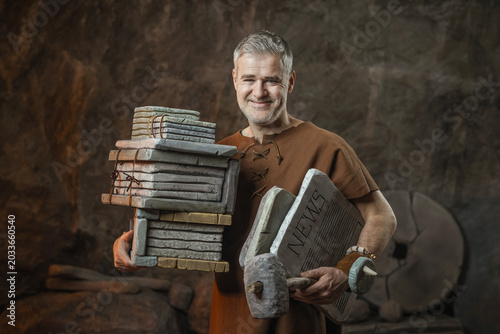 Fotografia Smiling Prehistoric Businessman Holding Stone Documents and News Tablet