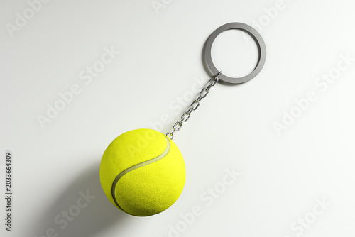 Bright tennis ball keychain suspended on a chain over an empty light backgrou...
