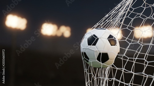 Close-up of a soccer ball caught in the net, signifying a goal scored during a night game under stadium lights