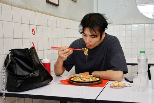 фотографія Young Asian Man Eating Spicy Noodles in Casual Restaurant