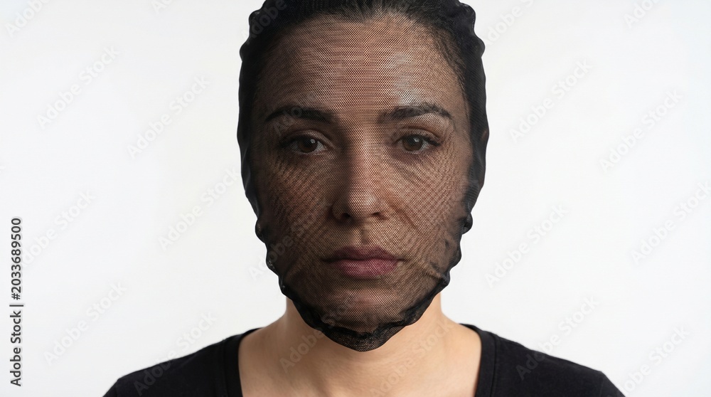 Obraz premium Close-up portrait of a woman with a serious expression, her face covered by a black mesh net against a plain white background.