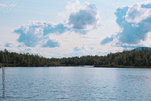 Tranquil Morning Lake Landscape in Swedish Lapland with Calm Water Deep Green Pine Forest Treeline and Majestic Mountain Silhouette under Overcast Sky 
