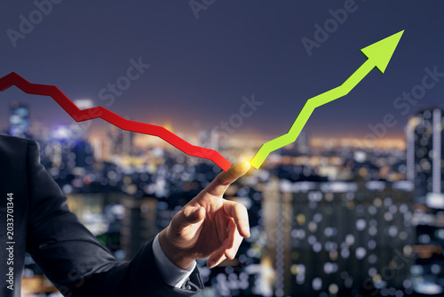Bild auf Leinwand Business person pointing at changing red downward line to green upward growth arrow over city lights at night symbolizing market turnaround
