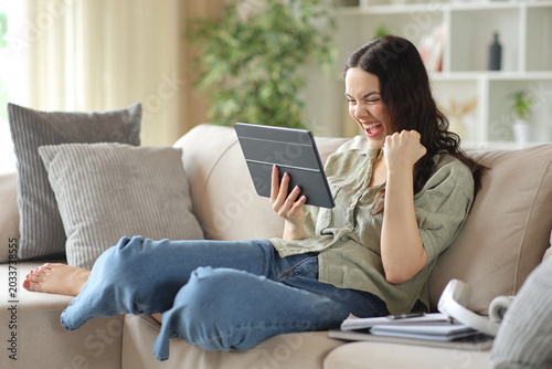 Excited student celebrating good news holding tablet