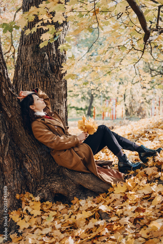 Woman rests against large tree trunk in autumn forest holding leaves with closed eyes. Grounding in nature autumn, Sensory Walking, Physical Earthing, Cycle of Letting Go.
