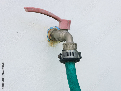 Fotografie A metal outdoor water faucet with a pink handle and a green rubber hose attached to a white wall
