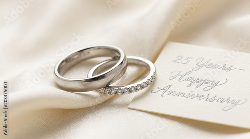Silver wedding rings for 25th anniversary celebration, elegant platinum bands on silk fabric, happy anniversary greeting card with calligraphy