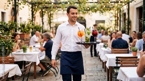 Waiter carries drinks in outdoor restaurant filled with guests enjoying their meals in warm weather