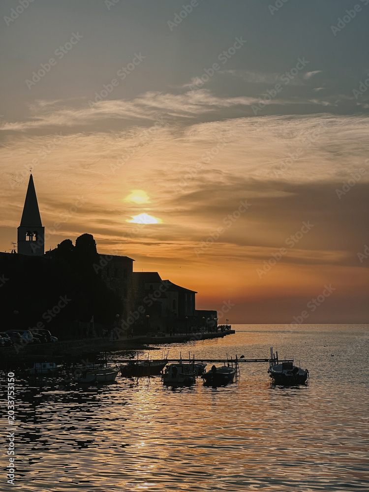 Obraz premium Sunset Over the Harbor with Silhouetted Buildings