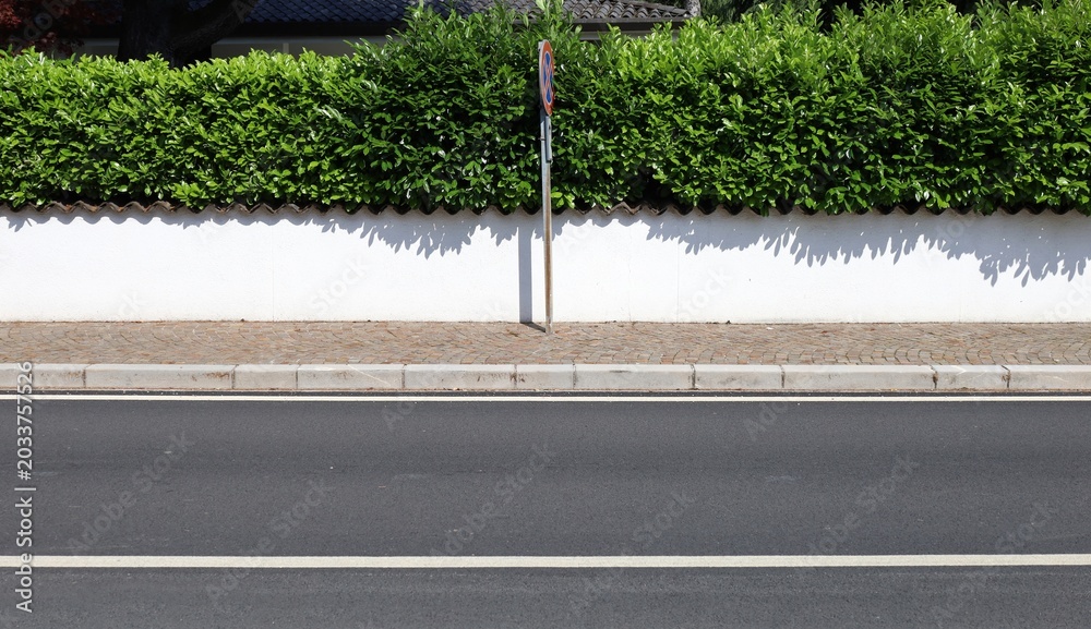 Φωτογραφία No stopping sign on sidewalk in front of a white plaster fence with hedge above