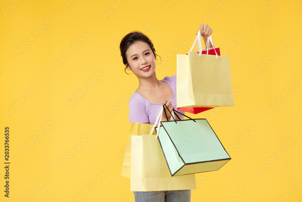 Fototapeta premium Smiling Woman Holding Shopping Bags on Yellow Background