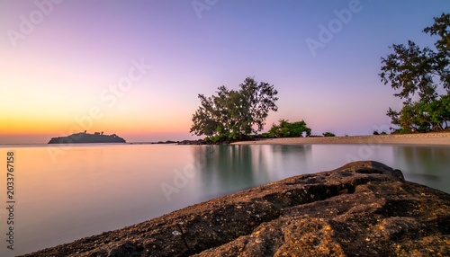 Serene coastal scene features a colorful sunset, island, and calm water