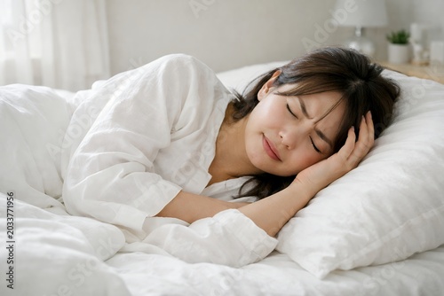 Plakat 白いベッドで横になりながら頭痛や体調不良で頭を抱えて悩むパジャマ姿の若い女性