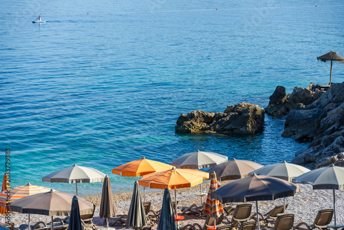 Quadro su tela Rows of colorful beach umbrellas and sun loungers on a rocky Adriatic beach with turquoise water in Croatia