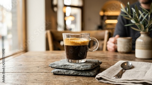 Clear glass cup of rich espresso on stone coasters, refined coffee still life for cafe branding, hospitality, morning routine and minimalist food styling, warm crema detail with elegant tabletop