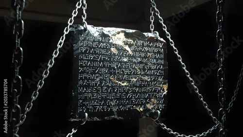 A vast suspended panel of carved obsidian inscribed with sacred law, hanging by iron links in a severe interior void where silence heightens the emotional force of the text, angled side illumination r