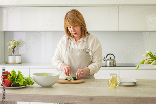 Mature woman chopping and cutting vegetable,  making breakfast. Preparation, cookery and healthy food concept. Woman 40s portrait