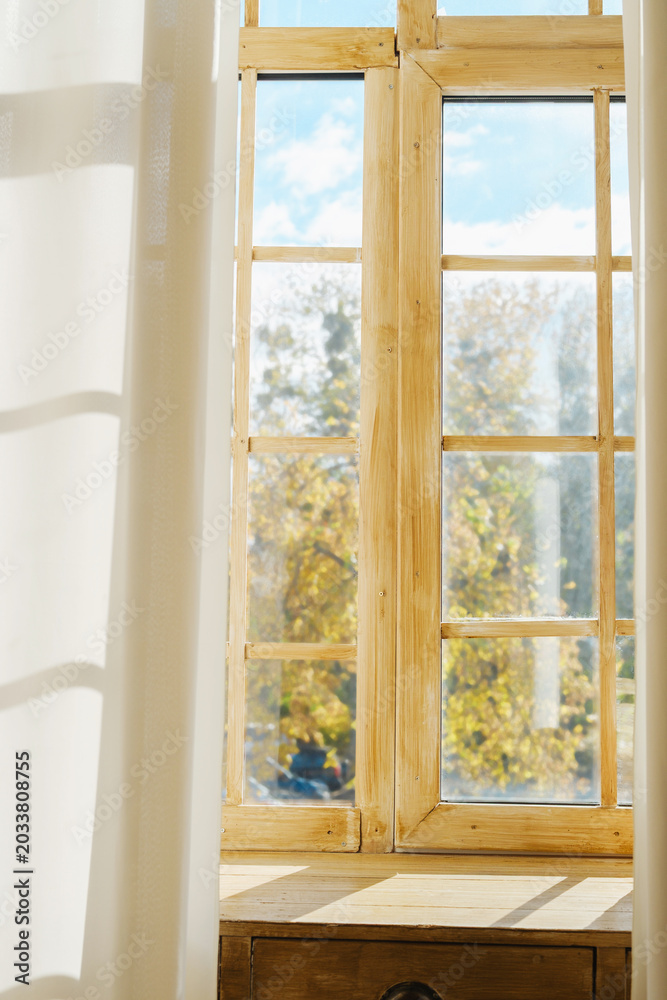 Fototapeta premium Warm light streams through rustic wooden window revealing autumn trees and blue sky.