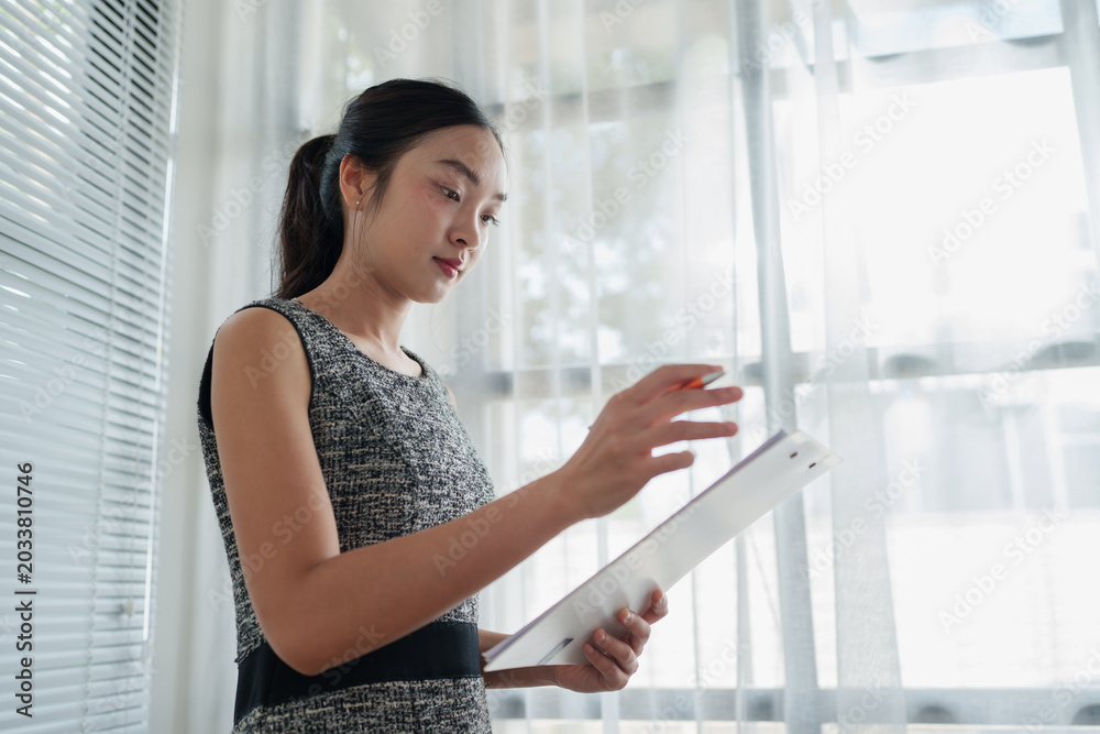 Fototapeta premium Asian businesswoman reviewing documents standing in modern office