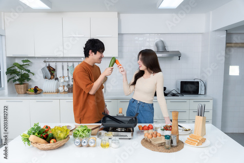 Happy portrait of loving young asian of having fun standing a cheerful preparing food and enjoy cook cooking with vegetables, meat, bread while standing on a kitchen Condo life or home