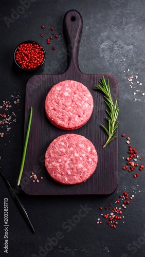 Two raw patties on wooden board with herbs