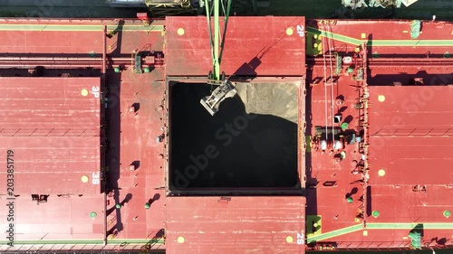 Unloading dry cargo ship of wheat by cranes in port. Aerial view loading into holds of sea cargo vessel