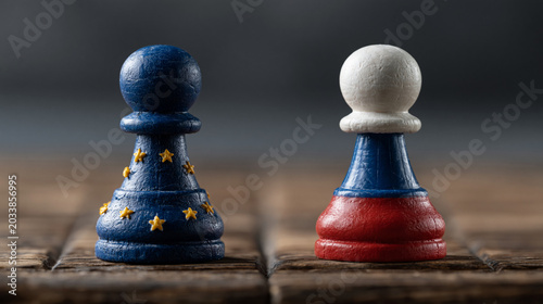 European Union and Russian Flag Pawns Facing Off: Two chess pawns, one adorned with the European Union flag and the other with the Russian flag, stand in opposition on a wooden surface.