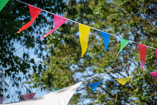 Konstfotografi Bunte Wimpelgirlanden hängen bei sonnigem Wetter zwischen Bäumen im Freien als f