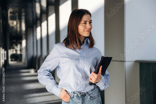 Canvastavla Young woman with brown hair wearing a light blue shirt and jeans stands confiden